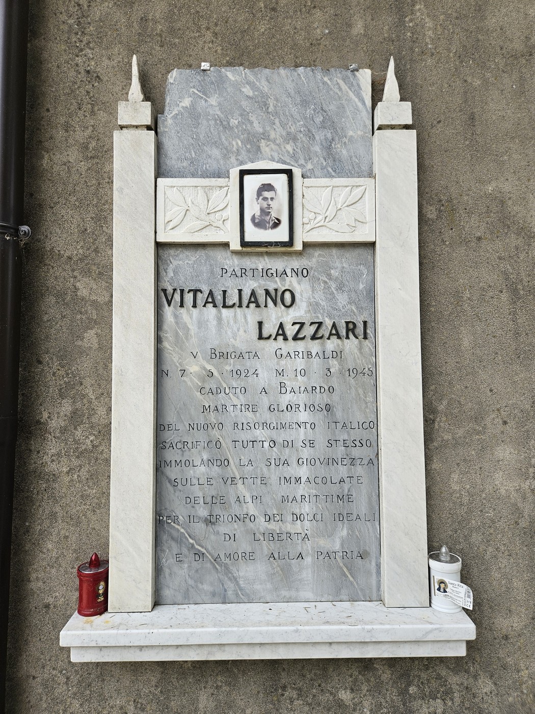 Lapide dedicata a Vitaliano Lazzari, partigiano caduto nel 1945, adornata da una fotografia e candele commemorative.