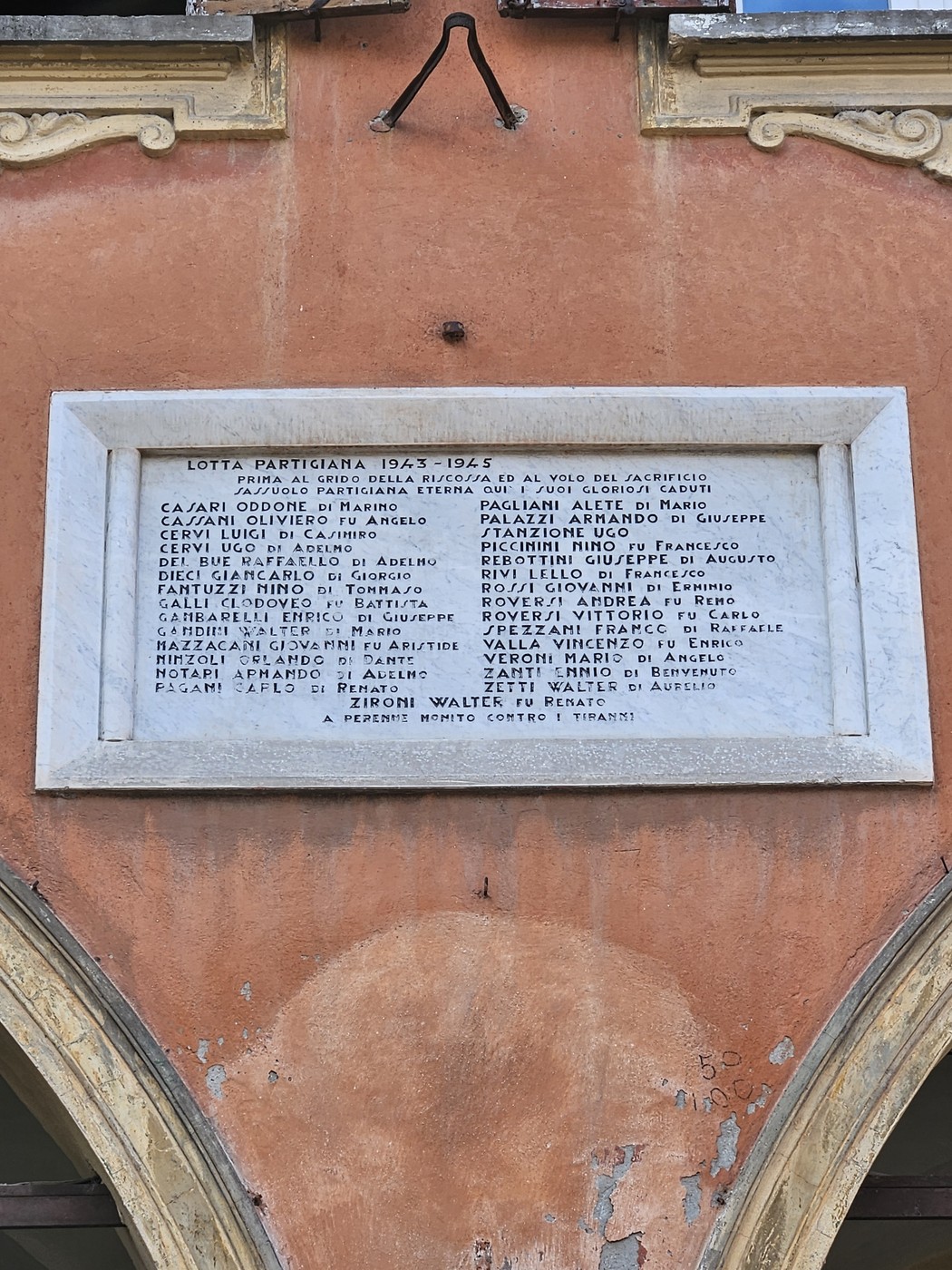 Lapide commemorativa dedicata ai partigiani caduti, affissa su un edificio storico.