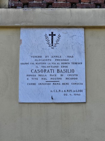 Lapide marmorea con croce e corona d'alloro incisa, fissata su parete esterna, con iscrizione dedicatoria.