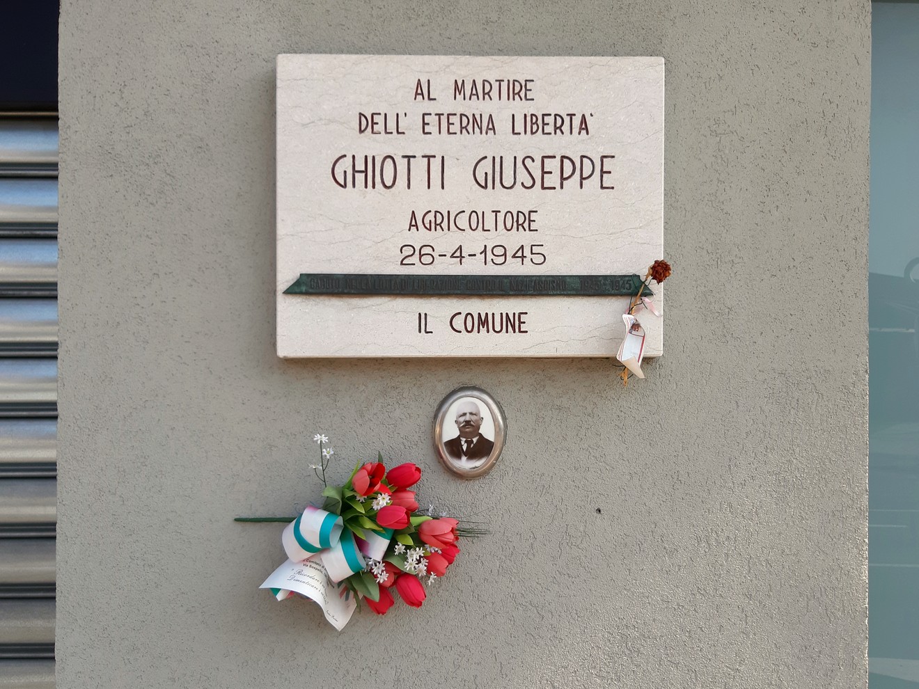 Lapide commemorativa di Giuseppe Ghiotti, martire per la libertà, con fiori e foto.