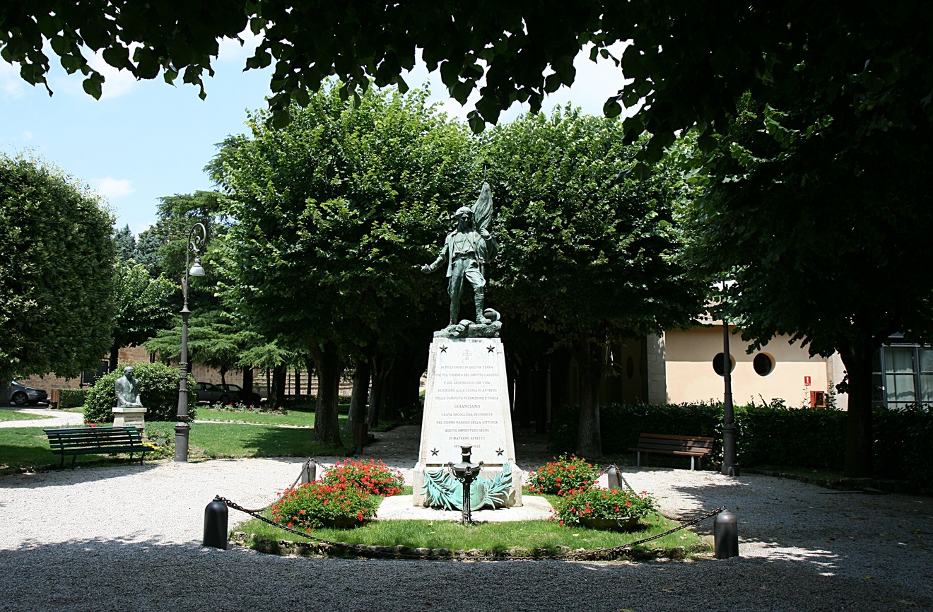 Monumento ai caduti circondato da alberi e aiuole fiorite in un tranquillo parco.