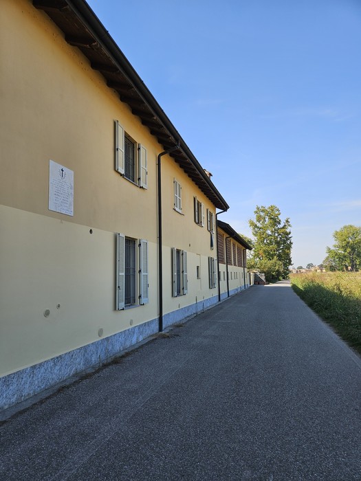 Lapide con iscrizione affissa sulla parete di un edificio lungo una strada di campagna.