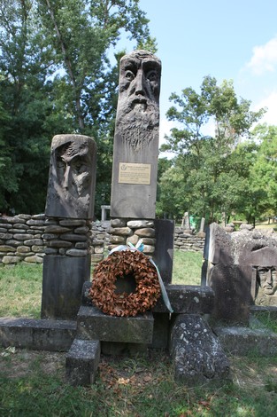 Monumento commemorativo con sculture artistiche e una corona di fiori in un'area verde.