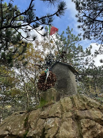Sacrario ai Martiri di Passo Mezzano, monumento su roccia con bandiera e corona di lauro circondato da alberi.