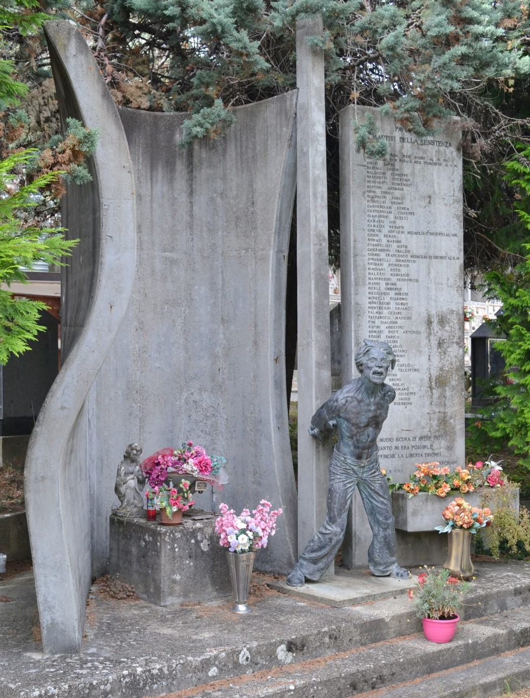 Monumento ai martiri della Resistenza a Pavullo, con statue e dedica ai caduti, circondato da fiori.