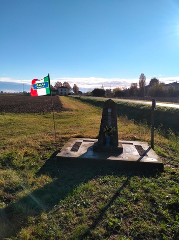 Cippo a Guidi con bandiera italiana, in un paesaggio rurale sereno e soleggiato.