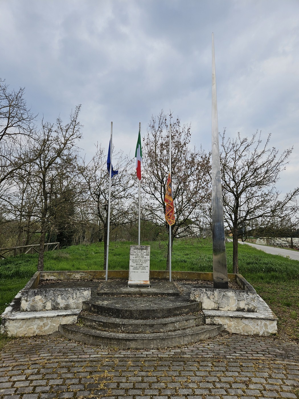 Monumento ai Martiri di Villamarzana con bandiere e struttura elegante circondata da alberi e verde.