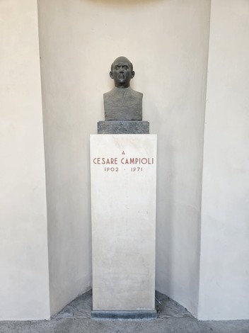 Busto di Cesare Campioli, affiancato da una base con iscrizione, in un ambiente sobrio e illuminato.