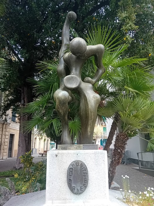 Monumento alla Resistenza, scultura moderna con figure stilizzate in bronzo tra vegetazione.