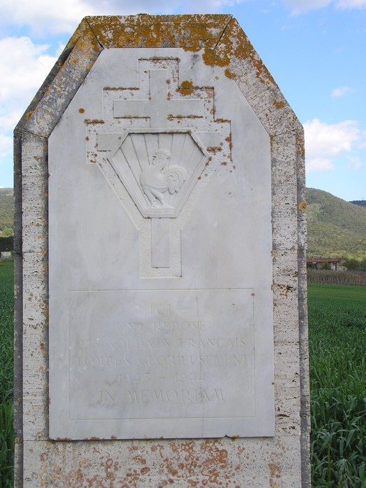 Cippo commemorativo dedicato ai caduti francesi, situato in un campo, con un simbolo religioso.