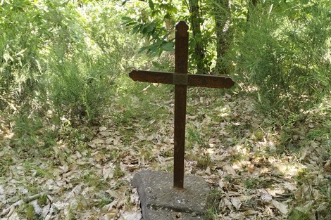 Croce di ferro in un'area verde, circondata da vegetazione e foglie secche.