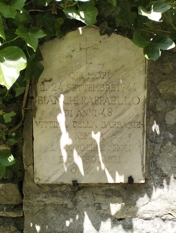 Lapide commemorativa dedicata a Bianchi Raffaello, vittima della barbarie nel 1944, posta in un contesto naturale.