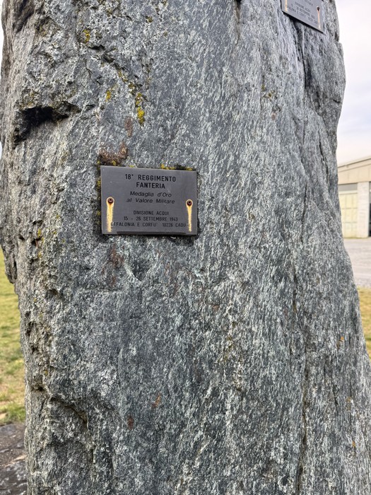Targa metallica con iscrizione fissata su un masso di pietra grezza all'aperto.