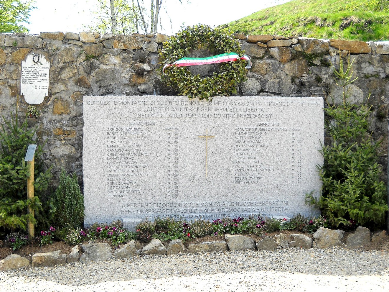 Lapide commemorativa ai caduti partigiani, decorata con una corona e un nastro tricolore.