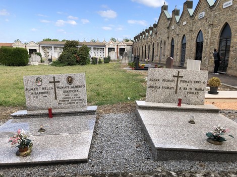 Sepolcro di Piumini, con lapidi commemorative e fiori, in un cimitero ben curato e luminoso.