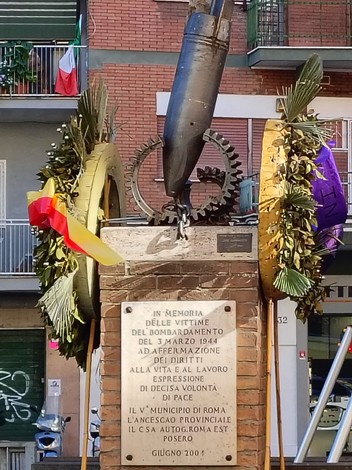 Monumento commemorativo dedicato alle vittime del bombardamento del 3 marzo 1944, adornato da fiori e un proiettile.