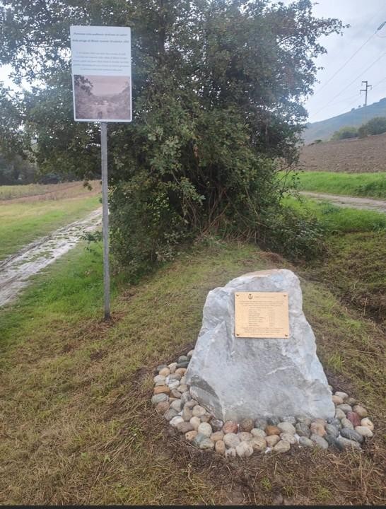 Monumento ai caduti di Monte Armato, situato in un'area verde con sassi decorativi e pannello informativo.