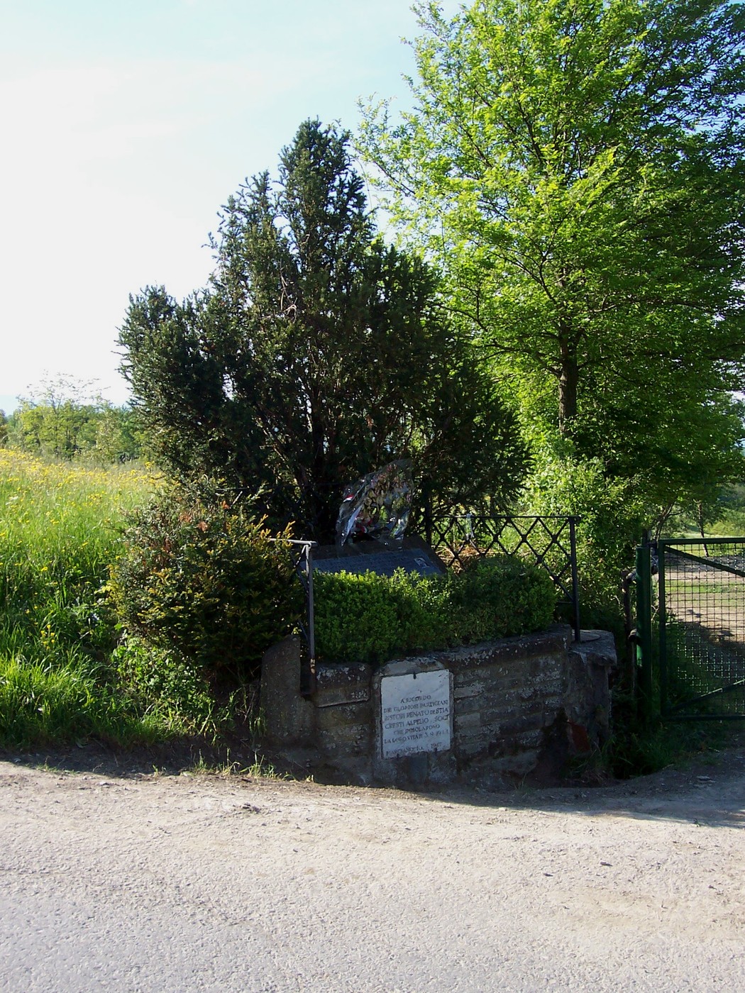 Monumento a Crespi e Ristori, immerso nel verde, con un breve monumento circondato da vegetazione e recinzione.