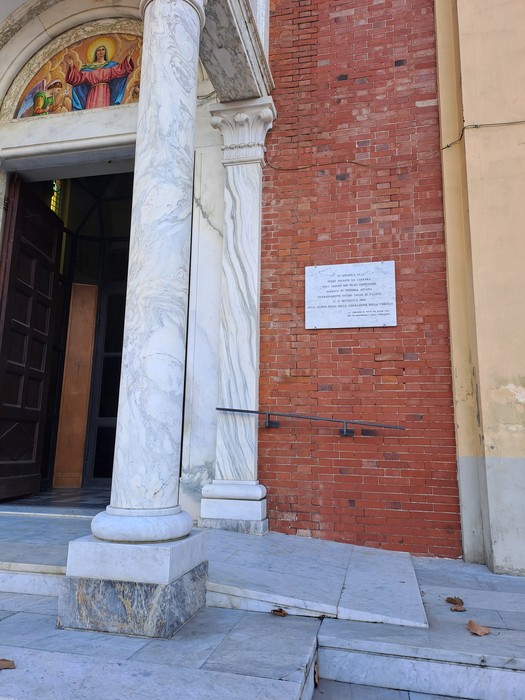 Lapide commemorativa a Rossi collocata accanto all'ingresso di un edificio religioso, con colonne e decorazioni.