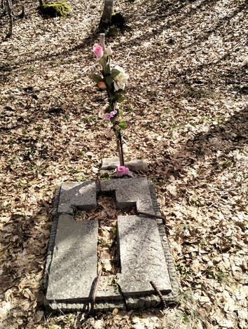 Cippo commemorativo avvolto da foglie secche e decorato con fiori, simbolo di memoria e rispetto.