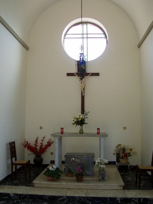 Interno della Cappella dei Caduti Partigiani, con altarino, croce e decorazioni floreali in un ambiente semplice e sobrio.