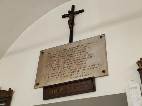 Lapide commemorativa dedicata ai volontari della Misericordia, con crocifisso superiore. Onore ai defunti.