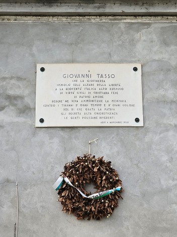 Lapide commemorativa dedicata a Giovanni Tasso, con una corona di foglie secche e un nastro.