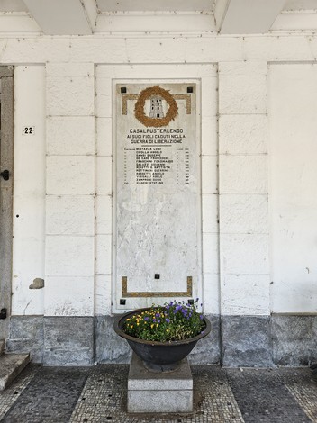 Lapide commemorativa ai caduti della guerra di Liberazione a Casalpusterlengo, con fiori decorativi.