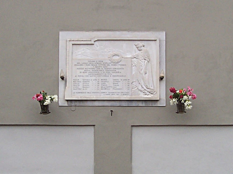 Lapide commemorativa dell'Istituto Farmaceutico Militare, decorata con fiori.