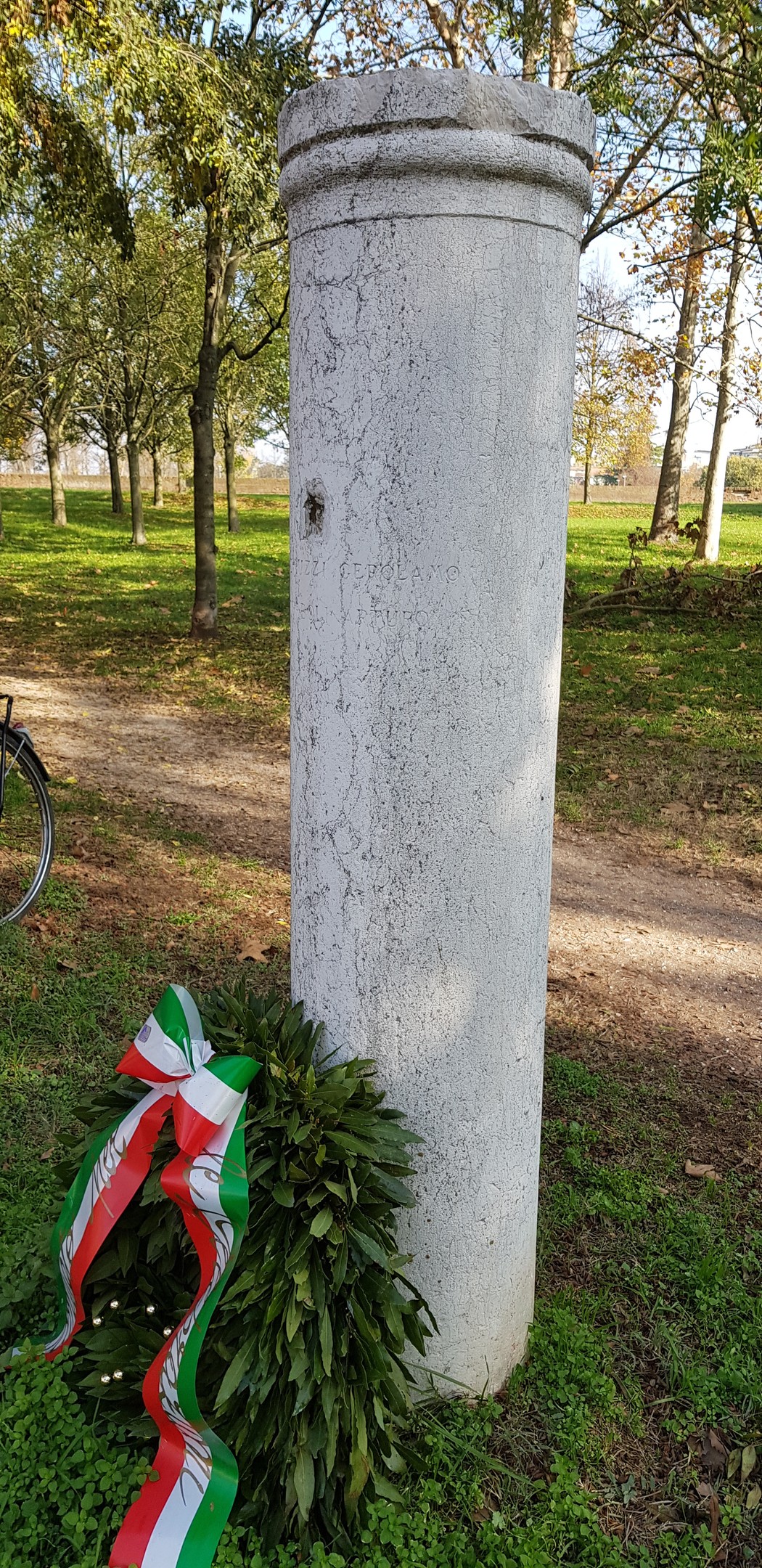 Colonna commemorativa a Savonuzzi, adornata con un'alloro e nastri tricolori, immersa nella natura.