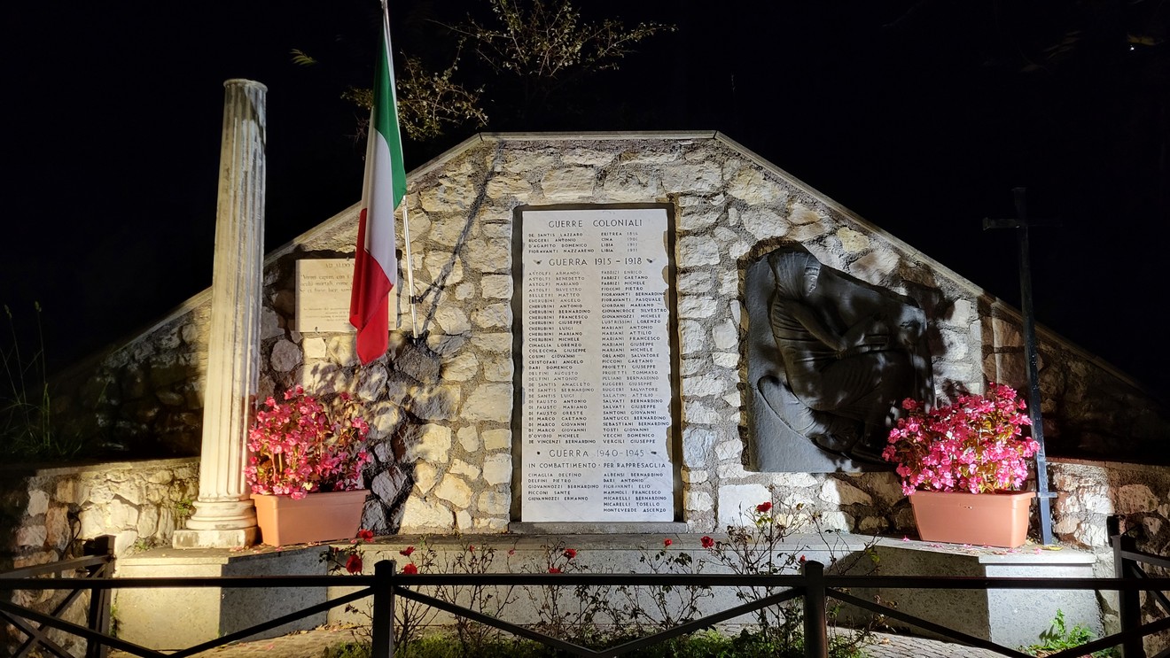 Monumento ai caduti di Rocca Canterano, dedicato alla memoria dei soldati, illuminato di notte tra fiori e bandiere.