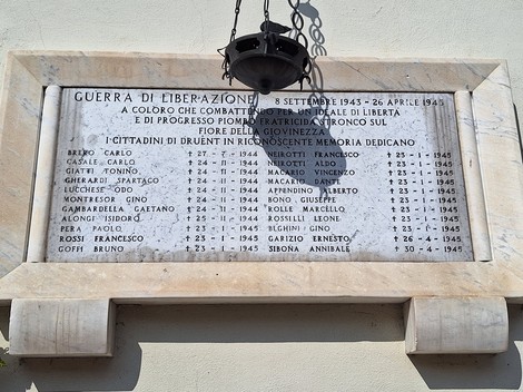 Lapide in marmo con lungo elenco di nomi e date, fissata su parete esterna, sormontata da lanterna.
