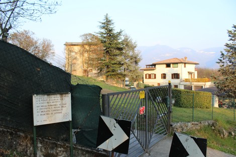 Ingresso alla villa della famiglia Volpi, circondata da vegetazione e colline sullo sfondo.