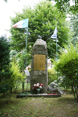 Monumento dedicato ai caduti del bombardamento, immerso nel verde, con bandiere e fiori a commemorare le vittime.