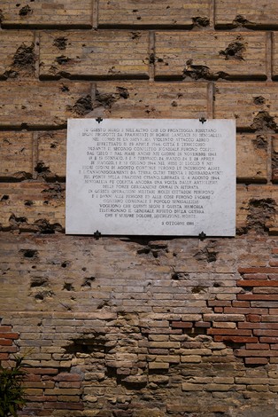 Lapide in memoria dei caduti durante i bombardamenti, affissa su un muro vissuto e segnato dal tempo.