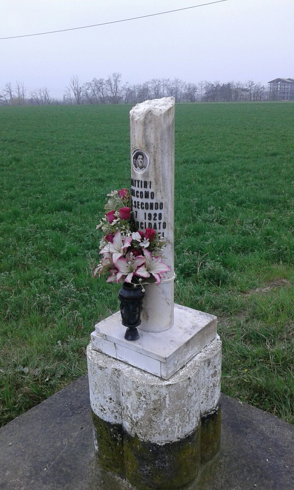 Cippo a Pattini: monumento commemorativo con fiori, immerso in un campo verde.
