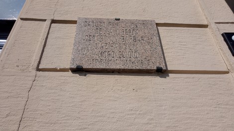 Lapide commemorativa in pietra dedicata a un evento storico, affissa su una parete.