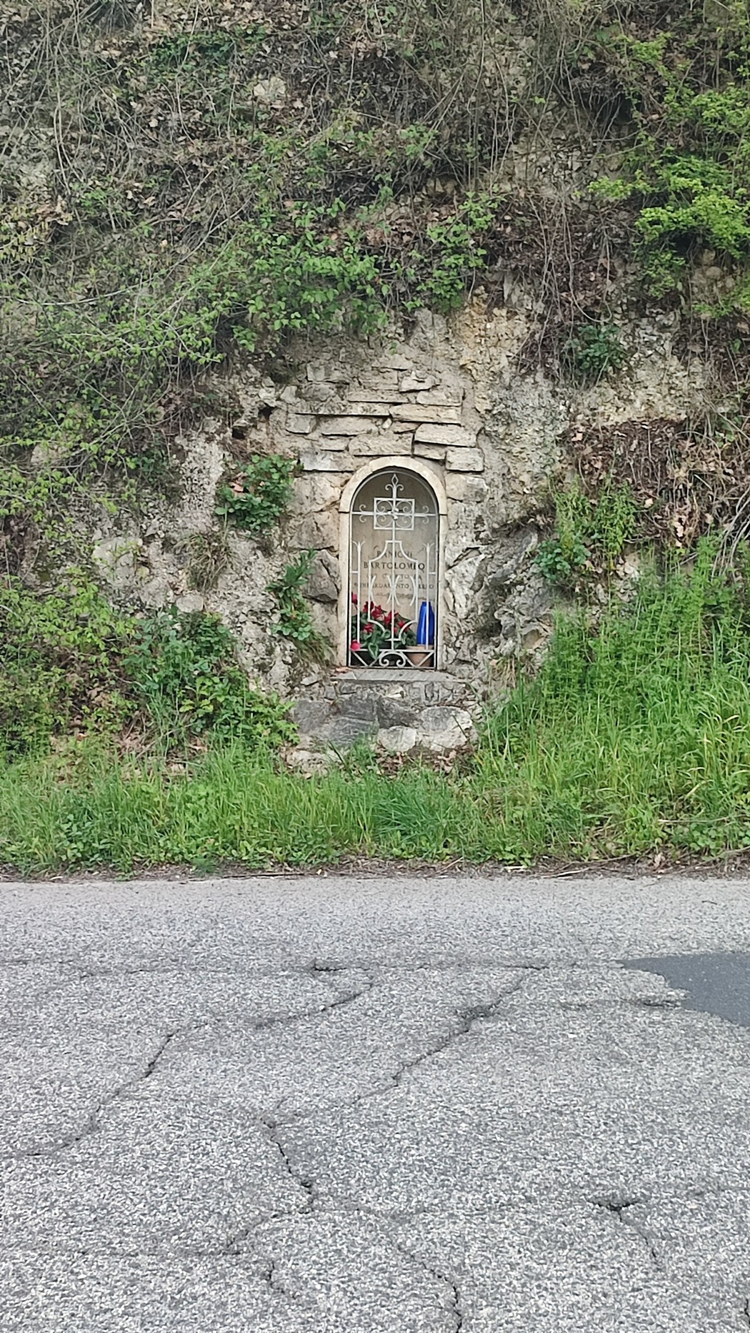 Edicola per Panichi incastonata nella roccia, circondata da vegetazione e fiori.