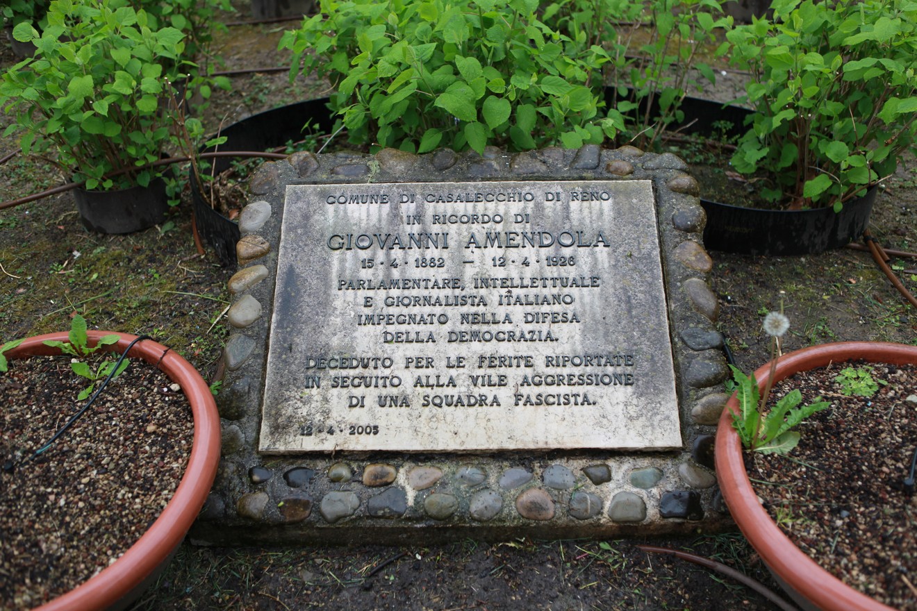 Lapide commemorativa dedicata a Giovanni Amendola, situata in un giardino con piante verdi circostanti.