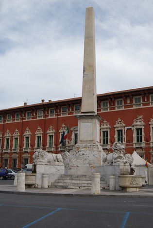 Obelisco dell'Unità d'Italia, monumento storico con leoni e basamento, situato in una piazza storica.