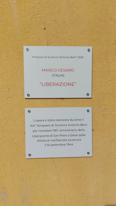 Due targhe bianche con iscrizioni su parete gialla, dedicate all'opera "Liberazione