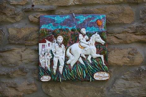 Lapide in ceramica decorativa che rappresenta la famiglia Tozzi con figure di contadini e un cavallo.