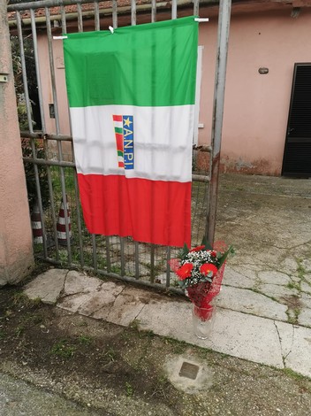 Pietra d'inciampo a Duranti con una bandiera italiana e un omaggio floreale vicino a un cancello.