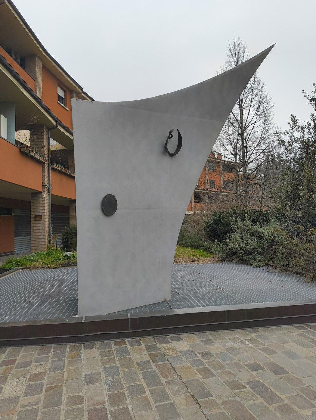Monumento a Piccinini, scultura moderna con forme geometriche e dettagli minimalisti, situato in un'area urbana.