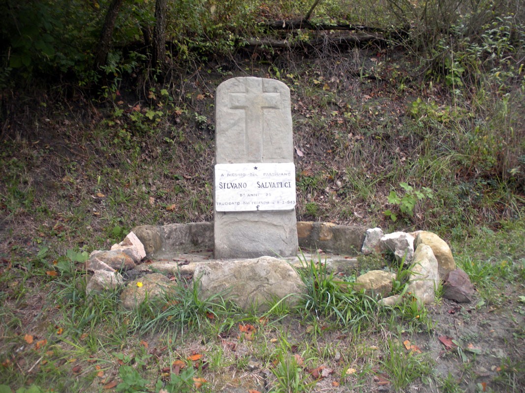 Cippo commemorativo in pietra dedicato a Salvatici, circondato da un piccolo recinto di sassi.