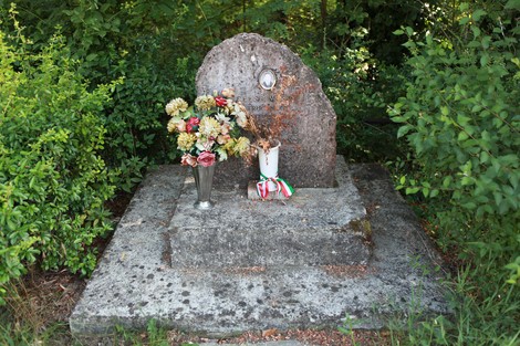 Monumento a Masini con fiori e un vaso, immerso nel verde circostante.