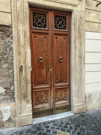 Porta in legno con dettagli ornamentali, tipica architettura di Dell'Ariccia, inserita in un contesto storico.