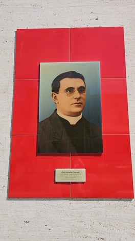 Targa commemorativa di don Giovanni Minzoni con un ritratto e un sfondo rosso, apposta su una parete.