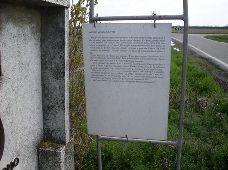 Cippo commemorativo dedicato ad Antonio Saccani, situato lungo un percorso stradale.