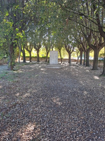 Monumento ai caduti di Pontasserchio, inserito in un ampio spazio verde con alberi e foglie sul terreno.